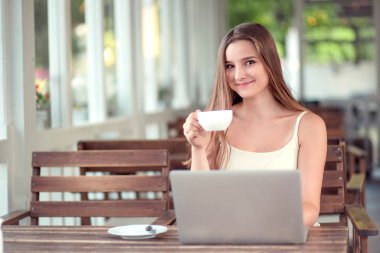 Dizüstü bilgisayar kullanırken elinde kahve ya da çay tutan kadın.