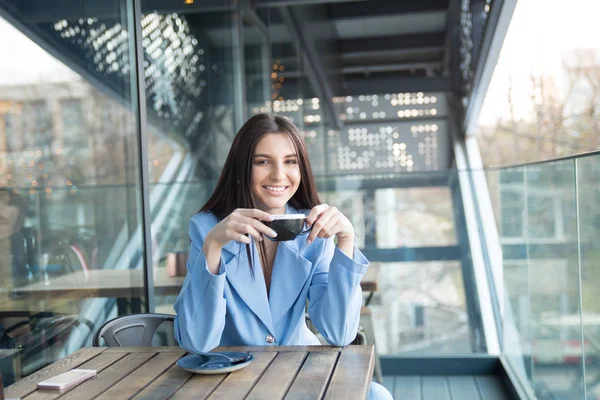 woman sitting at the balcony of cafe holding cup of hot tea.