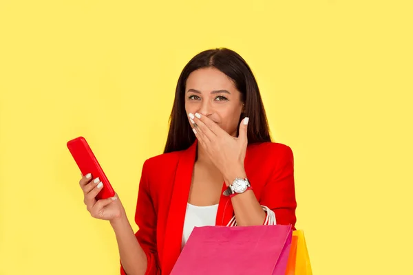 woman with shopping bags looking at phone laughing
