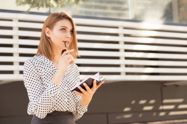 Not defteri ile çekici genç kadın öğrenci uzak düşünceli hayal bakıyor. Uzun bob saç kesimi ile resmi giyim ofisi veya kolej yakınında açık havada oturan kız