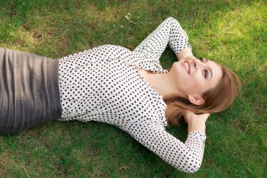 Dışarıda hayal kuran kadın. Rahat genç kişi başının altında elleri ile genç kız yukarı gülümseyerek mutlu açık havada resmi giyim yeşil çim çim kampüsünde ofisinin yanında yatarak bakıyor