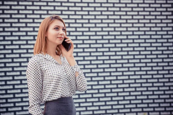 Talking. Closeup portrait headshot young pretty businesswoman in formal wear holding cellphone discussing on mobile making appointments by phone standing in front of a white black brick wall