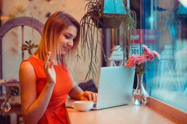 Gülümseyen bir kadın öğrenci, video görüşmesi yapan serbest çalışan, ev mutfağındaki bir dizüstü bilgisayarla röportaj yapan, pencerenin yanında ya da kahve dükkanında, beyaz benekli kırmızı elbise giyen moda bir kafe..