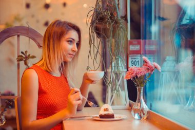 Düşünceli bir kadın tatlı bir tatlı yerken hayal kuruyor ve evinin mutfağında çay içiyor, pencerenin yanında ya da kahve dükkanında, beyaz benekli kırmızı elbise giyen şık bir kafe.