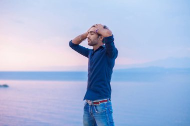 Mavi gökyüzüne gülümseyen bir adam gün batımında özgürlük denizini kutlarken derin bir nefes alıyor. Pozitif duygu yüz ifadesi başarı hissi barış zihin konsepti. Özgür mutlu adam doğanın tadını çıkarıyor.