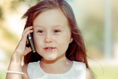 Telefonda konuşan kız. Güzel, çekici küçük bir kız dışarıda izole edilmiş cep telefonuyla arkadaşlarıyla sohbet ediyor. Olumlu insan yüzü ifadesi duygusu. Çocuk teknolojisi kavramı