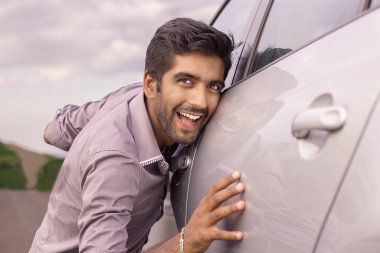 Mutlu, genç, esmer, İtalyan bir sürücü dışarıda arabasını okşuyor. Yeşil enerji biyoyakıt elektrik çevre dostu yeni araba konsepti. Olumlu yüz ifadesi insani duygu tepkisi