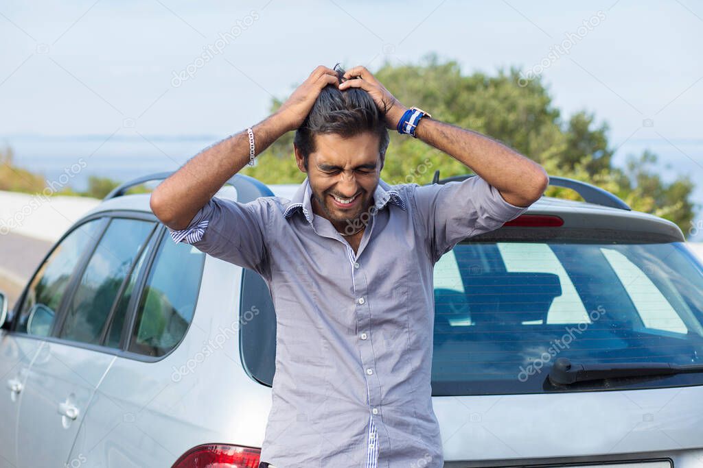 Upset driver after car accident crying hands on head, or he forgot the key while standing outdoors near his car, green tree blue sea and sky on background
