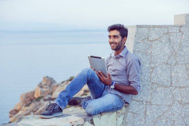 Mavi gökyüzüne bakarken mutlu gülümseyen bir adam denizin üzerindeki beton bir köprüde oturup arka planda günbatımı denizinde özgürlüğün tadını çıkarırken. Neşeli, heyecanlı, havalı biri.