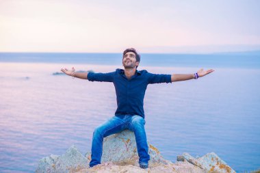 Mavi gökyüzüne gülümseyen bir adam gün batımında özgürlük denizini kutlarken derin bir nefes alıyor. Pozitif duygu yüz ifadesi başarı hissi barış zihin konsepti. Özgür mutlu adam doğanın tadını çıkarıyor.