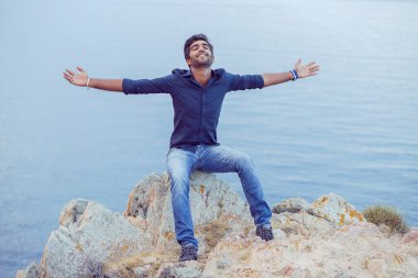 Mavi gökyüzüne gülümseyen bir adam gün batımında özgürlük denizini kutlarken derin bir nefes alıyor. Pozitif duygu yüz ifadesi başarı hissi barış zihin konsepti. Özgür mutlu adam doğanın tadını çıkarıyor.