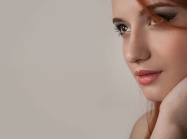 Kızıl saçlı bir kadın portresi. Güzel kızıl saçlı kız elleriyle yüzünü okşamaya çalışıyor, seksi ve güzel makyajlı. Gri bej arka planda izole edilmiş çok ırklı beyaz İspanyol kadın güzellik modeli.