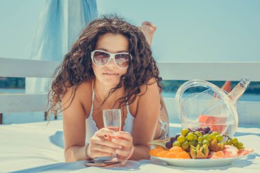 Yakından bakınca, güzel bir kadın elinde bir kadeh şampanya tutarak mutlu bir şekilde gülümsüyor. Yıldönümünü kutluyor. Yeni yıl, açık havada, tropik adadaki deniz gölü kumsalında güneşleniyor. Pozitif ifade