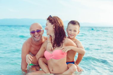 Şirin bir aile sahilde eğleniyor, açık havada birlikte oynuyorlar, arka planda mavi deniz suyu, açık havada.