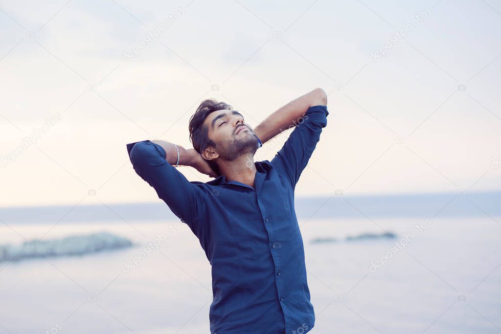 Man smiling looking up to blue sky taking deep breath celebrating freedom sea background at sunset. Positive emotion face expression feeling success peace mind concept. Free happy guy enjoying nature