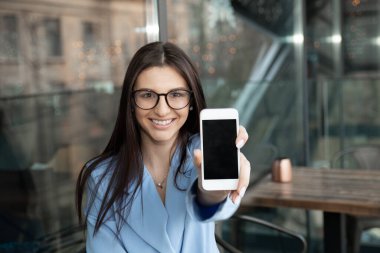 Telefon konseptime bak. Teras balkonundaki masada oturan boş bir siyah ekranı gösteren akıllı bir telefonu olan mutlu bir Latin iş kadınının yakın plan portresi. Telefona odaklan.
