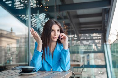 Evinin balkonunda ya da kahve dükkanının terasında mavi takım elbiseli modaya uygun bir kafede otururken telefonda konuşan mutsuz, hayal kırıklığına uğramış bir kadın. Olumsuz duygu yüz ifadesi hissi
