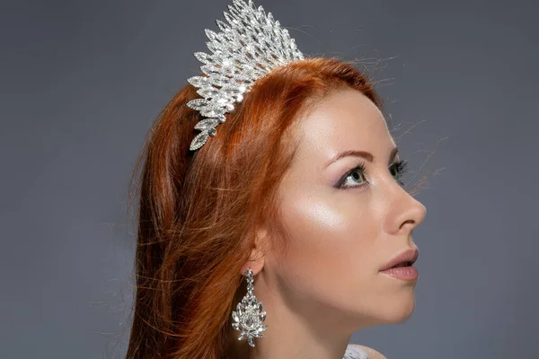 Beauty queen. Woman in profile with diamond crown on head looking up to side posing isolated on grey background. Multicultural Caucasian Irish model
