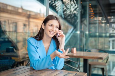 Güzel, mutlu bir kadının telefondaki portresi mutlu bir şekilde gülümseyen ev mutfağındaki kameraya bakan, evinin yakınındaki bir balkonda ya da bir kafede mavi takım elbiseli moda bir kafe..