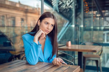 Mutsuz, hayal kırıklığına uğramış bir kadın telefonu elinde tutuyor, konuşmak istemiyor, kahve dükkanının terasında masada oturuyor, modaya uygun kafe balkonunda mavi takım elbise giyiyor. Olumsuz duygu yüz ifadesi hissi