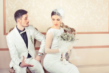 Kızgın gelin ve damat, birbirine kızmış bir erkek ve kadın koltuklarda oturup klasik arka planda izole edilmiş tarafa bakıyor. Gelin ve damat arasındaki anlaşmazlık