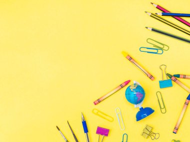 Okula dönmek, eğitim kavramı. Çok renkli kırtasiye araçları tebeşir, makas, küre, ataç, silgi, kalem, sarı arkaplanda izole edilmiş kalem, kenarda kopyalama alanı. Düz yatış, üst görünüm