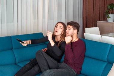 Evdeki mavi kanepede oturmuş televizyon izleyen mutlu bir çift.