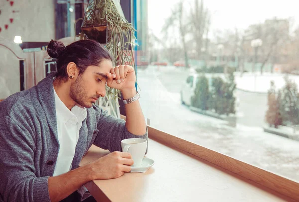 Stress. Portrait stressed sad young man with coffee cup sitting in a trendy cafe coffee shop about to cry. City urban life style stress. Negative human emotion face expression body language attitude.