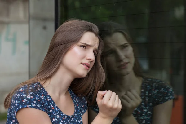 悲伤的年轻女子靠在现代建筑的玻璃墙上 望向远方的城市街道 — 图库照片