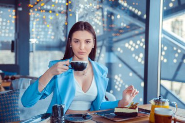 Manhattan 'da tatlı yiyip kahve içen genç ve güzel bir kadın resmi. İspanyol kız resmi mavi takım elbise giyiyor. Kafe terasındaki balkonda oturuyor. Arka planda.