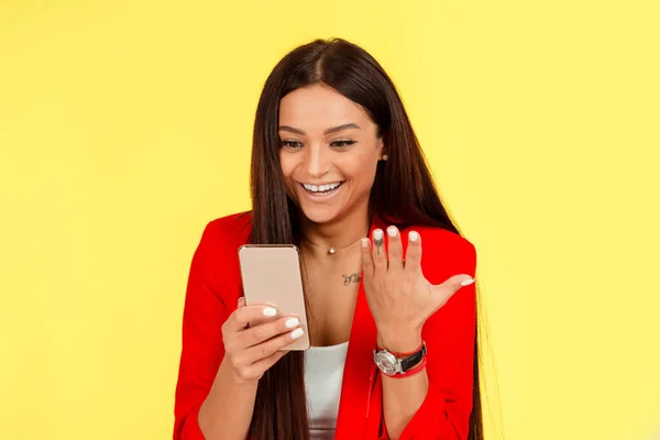 快乐的年轻女人在手机上看到朋友的短信 对好消息表示高兴 情绪激动的女人因为在黄色工作室的背景下购物而赢得打折 图库图片
