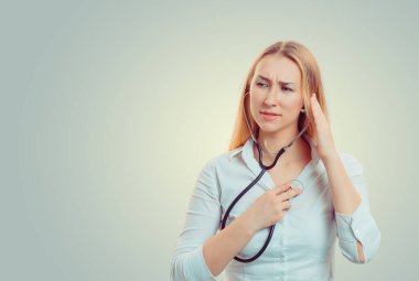 Beyaz tişörtlü genç, sarışın bir kadın üzgün üzgün bir şekilde bakarken steteskopu beyazdan izole edilmiş kalbini dinliyor. Negatif insani duygu, yüz ifadesi...