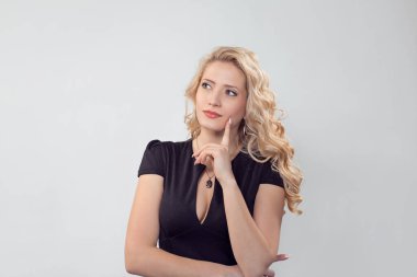 Siyah elbiseli çekici sarışın kadın hayal kuruyor ve hayallere dalıyor. Beyaz iş adamı, siyah resmi elbiseli, uzun sarı kıvırcık saçlı açık gri stüdyo arka planında izole edilmiş.