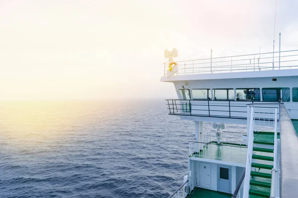 Cruise ship white cabin with big windows. Wing of running bridge of cruise liner. White cruise ship on a blue sky with radar and navigation system. Captain\'s cabin. Ocean sunset background.