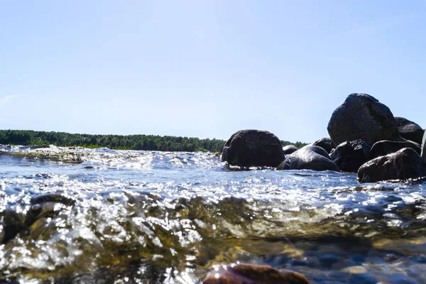 Big windy waves splashing over rocks. Wave splash in the lake against beach. Waves breaking on a stony beach, forming a spray. Water splashes. Water surface texture