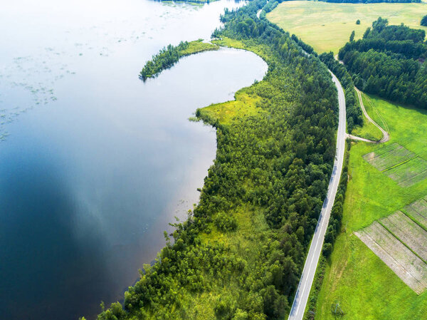 Вид с воздуха на шоссе. Вид с воздуха на проселочную дорогу возле озера. Проезжала машина. Воздушная дорога. Вид с воздуха. Захвачен сверху беспилотником. Мягкое освещение
