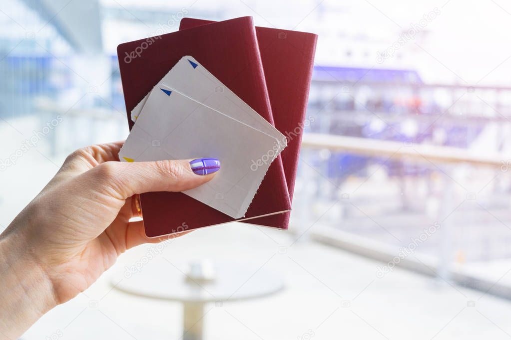 Closeup of beautiful woman hand holding passports and boarding pass tickets at airport terminal. Travel and holiday concept. Terminal lounge. Empty space. Copy space.