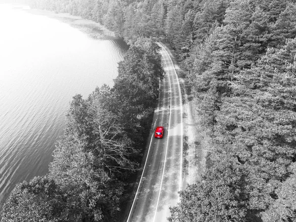 Aerial view of highway. Aerial view of a country road with moving red car. Car passing by. Aerial road. Aerial view flying. Captured from above with a drone. Black and white. Car in motion