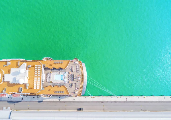 Aerial View by Drone of Cruise ship at harbor. Top view of beautiful large white liner in yacht club. Luxury cruise in sea water. Marina dock. Ship is moored at the quay. Turquoise water