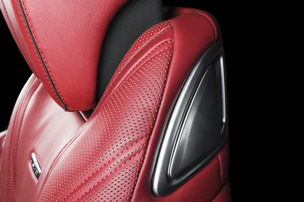 Red leather interior of the luxury modern car. Perforated red leather comfortable seats with stitching isolated on black background. Modern car interior details. Car detailing. Car inside