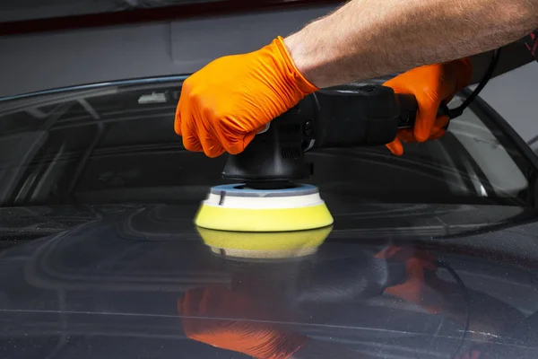 Car polish wax worker hands applying protective tape before polishing. Buffing and polishing car. Car detailing. Man holds a polisher in the hand and polishes the car. Tools for polishing