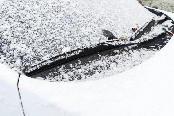 Snow covered car window with wipers, macro, close up. Car wiper blades clean snow from car windows. Flakes of snow covered the car.