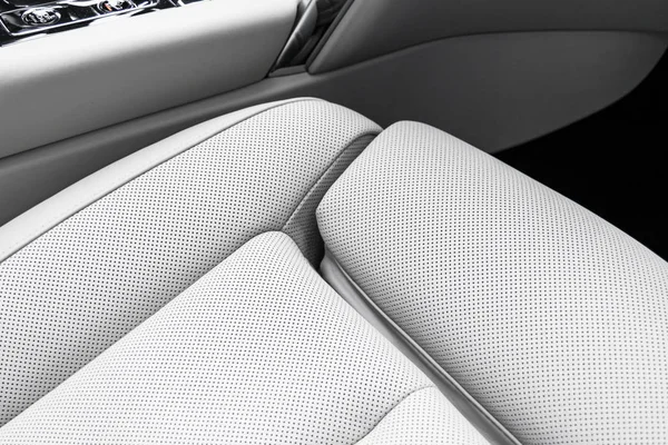 Modern luxury car white leather interior with natural wood panel. Part of leather car seat details with stitching. Interior of prestige modern car. White perforated leather. Car detailing. Car inside