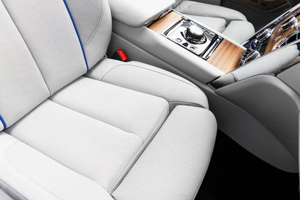 Modern luxury car white leather interior with natural wood panel. Part of leather car seat details with stitching. Interior of prestige modern car. White perforated leather. Car detailing. Car inside