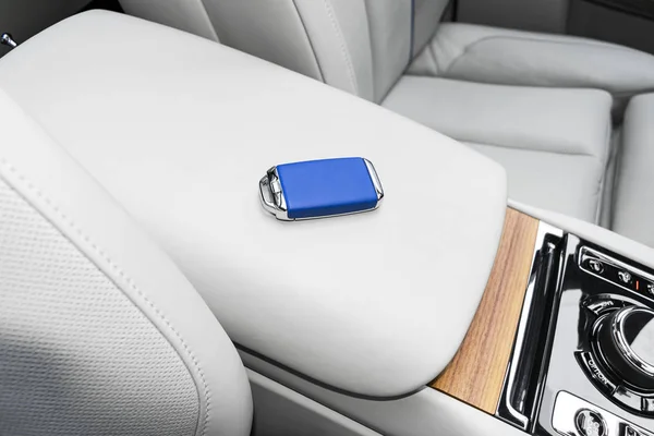 Closeup inside vehicle of wireless blue leather key ignition on natural wood panel. Wireless start engine key. Car key remote isolated. Modern Car keys detailing. Car keys close up. White perforated leather interior