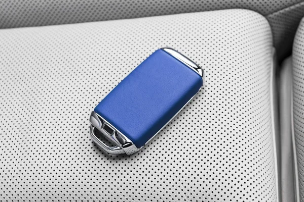 Closeup inside vehicle of wireless blue leather key ignition on white leather seat. Wireless start engine key. Car key remote isolated. Modern Car keys. Car keys close up. White perforated leather interior