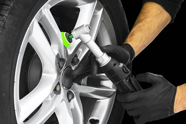 Car polish wax worker hands polishing car wheel. Buffing and polishing car disc. Car detailing. Man holds a polisher in the hand and polishes the car.
