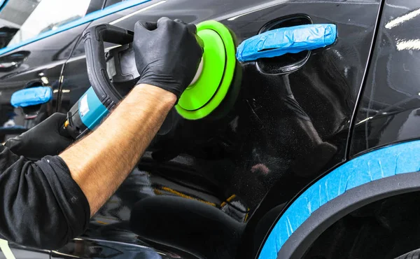 Car polish wax worker hands applying protective tape before polishing. Buffing and polishing car. Car detailing. Man holds a polisher in the hand and polishes the car