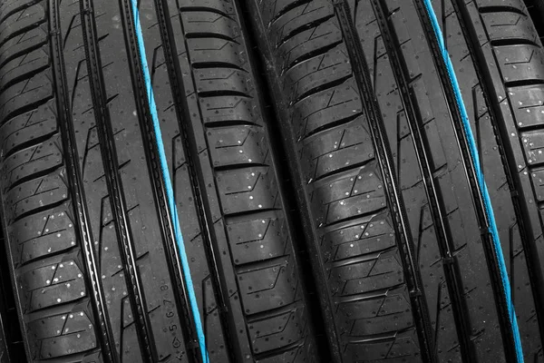 Studio shot of a set of summer car tires on black background. Tire stack background. Selective focus. Car tyre protector close up. Black rubber tire. Brand new car tires. Close up black tyre profile. Car tires in a row