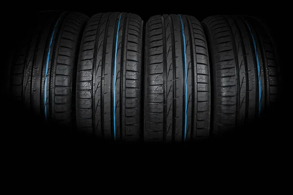 Studio shot of a set of summer car tires on black background. Tire stack background. Car tyre protector close up. Black rubber tire. Brand new car tires. Close up black tyre profile. Car tires in a row